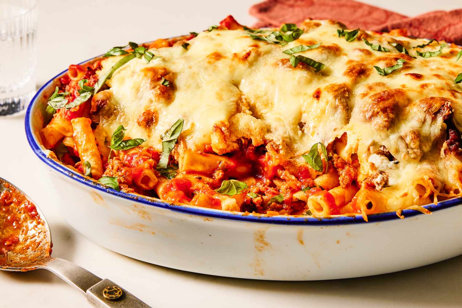 Baked ziti pasta in a casserole with melted cheese and herbs on top