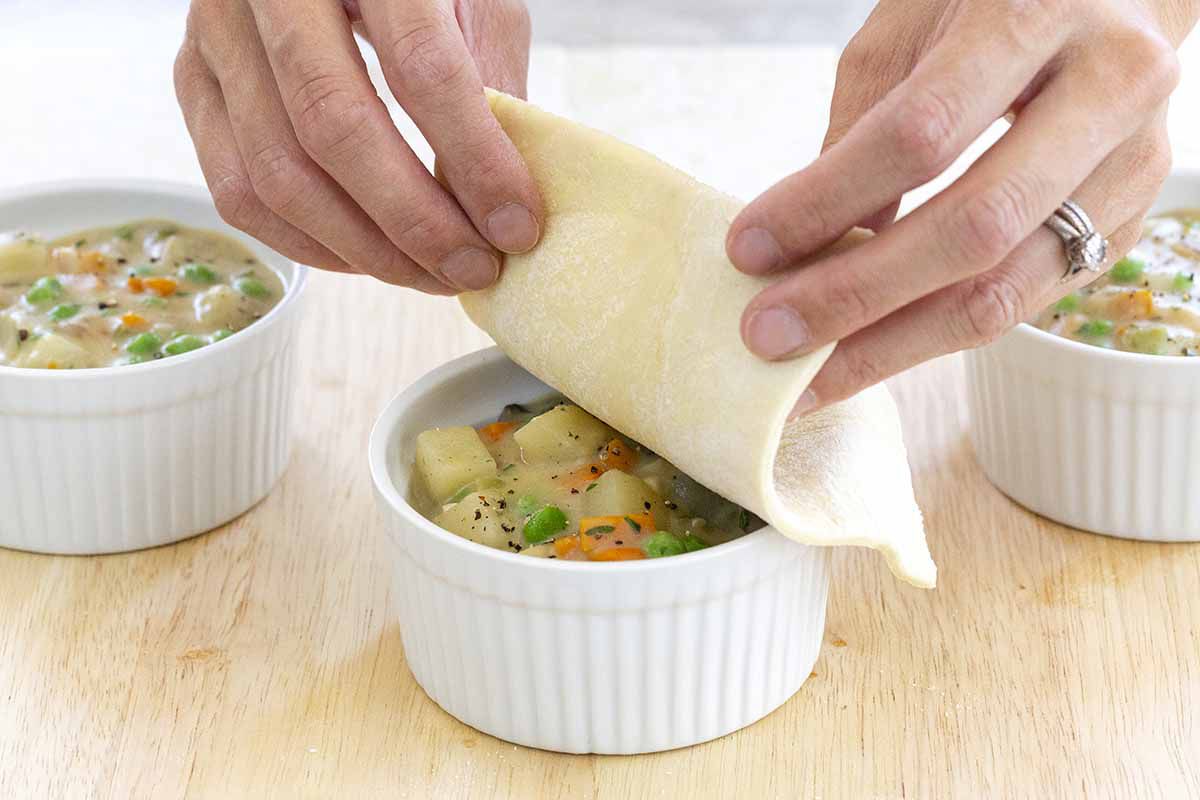 Puff pastry sheets being placed on top vegetarian pot pies.
