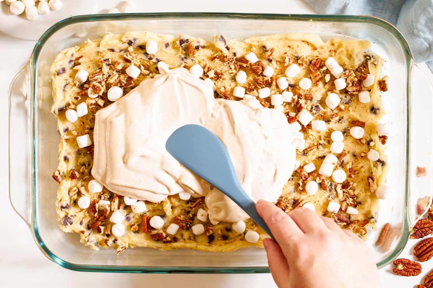 Egg white mixture for meringue getting spread over cookie dough base in a baking dish with a gray spatula for mud hen bars recipe