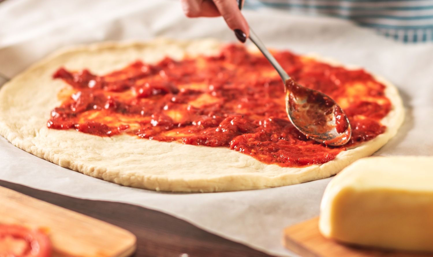 A person spreading tomato sauce on pizza dough with a spoon