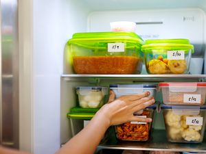 A hand reaching into a refrigerator storing labeled food containers