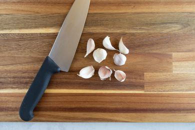 Garlic cloves with a chef's knife on a wood cutting board