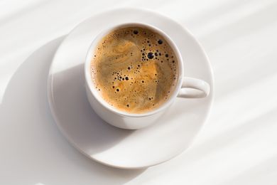 Overhead view of a cup of coffee and a white saucer on a white background