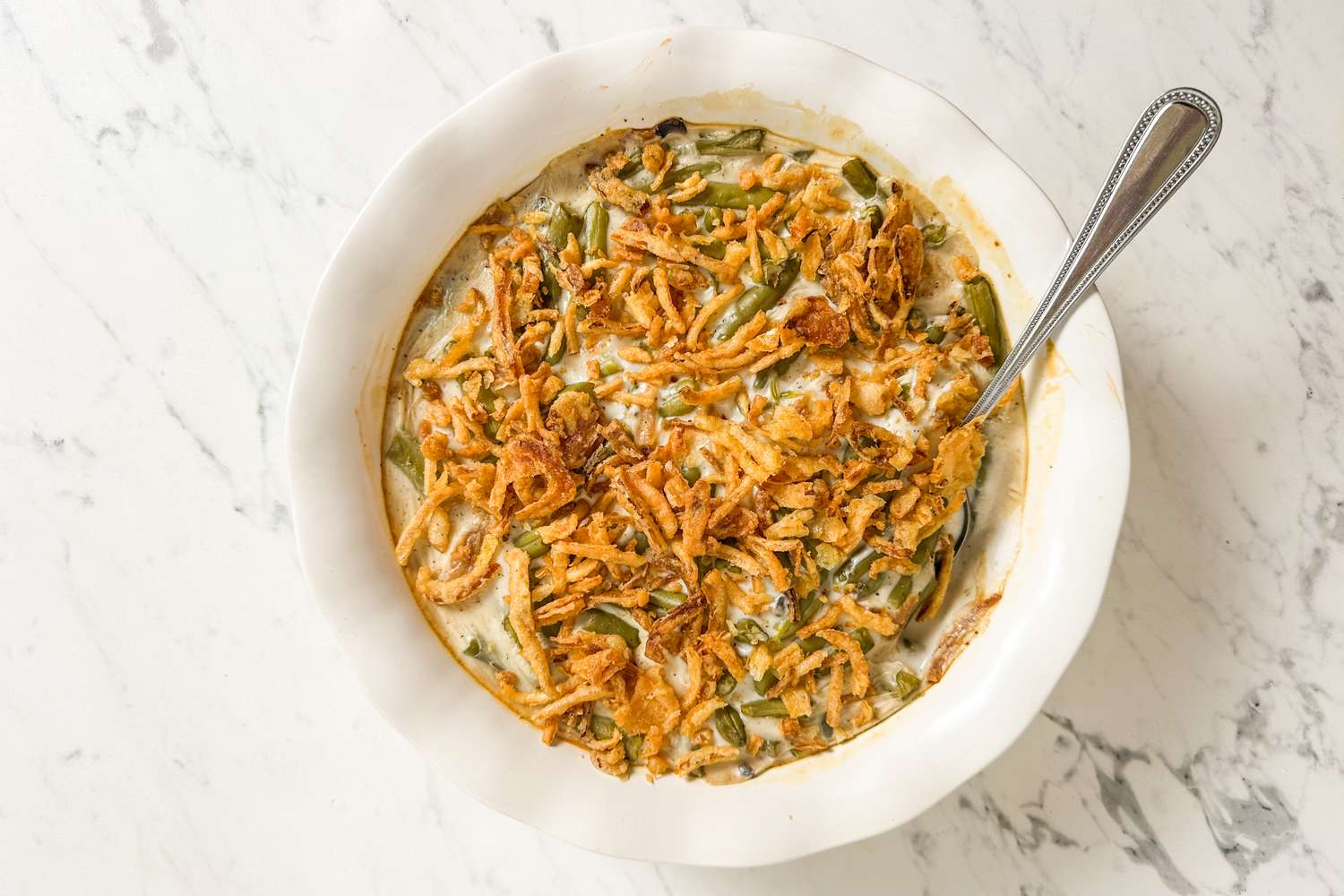 Green bean casserole topped with crispy fried onions served in a white dish with a spoon