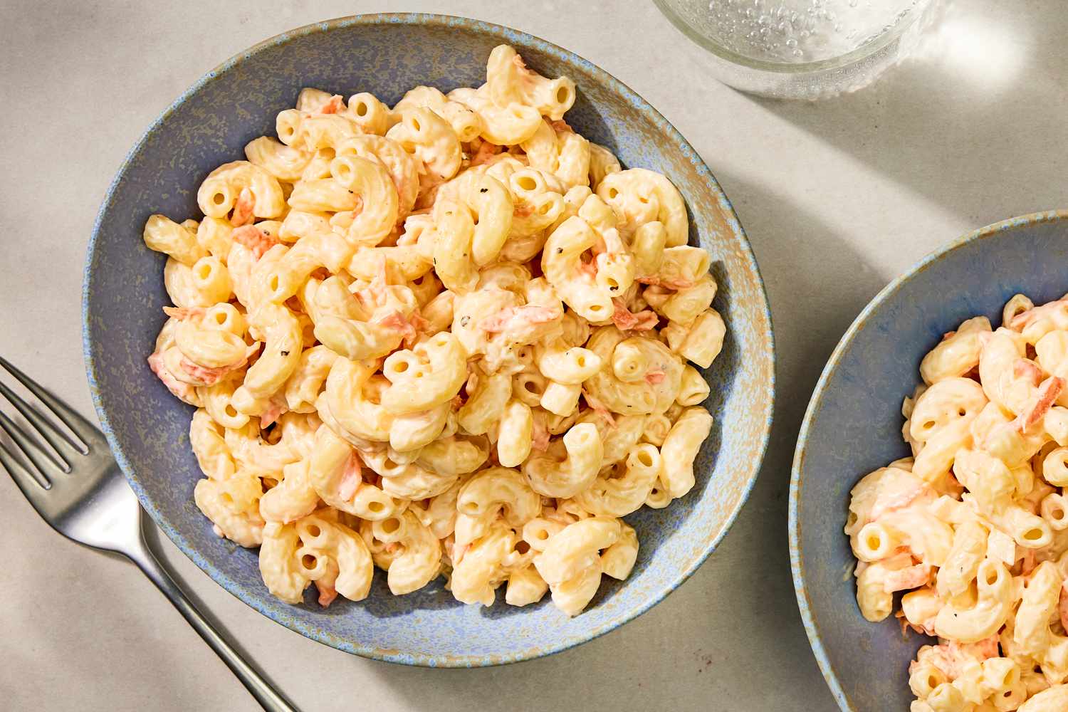 Hawaiian-style macaroni salad in a bowl, placed next to another bowl and a fork on a table