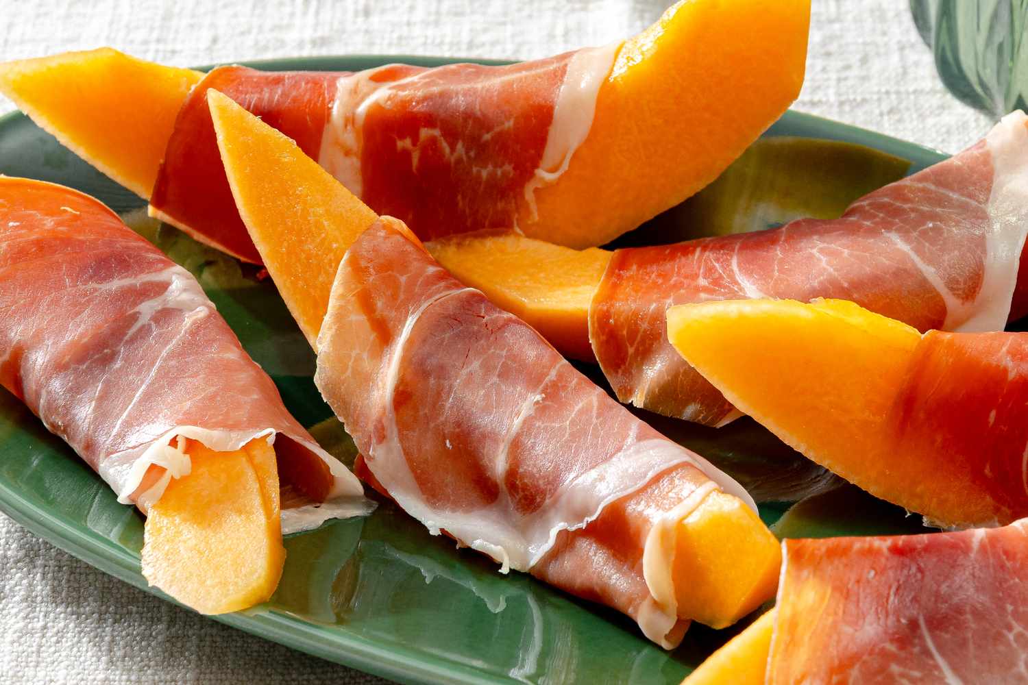 Slices of cantaloupe wrapped in prosciutto on a green plate
