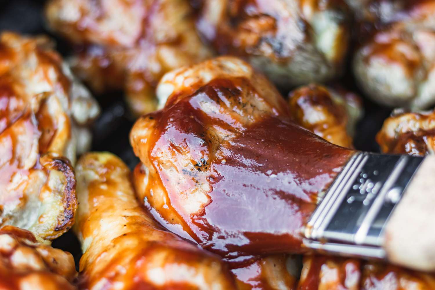 Brushing bbq sauce on grilled chicken thighs.
