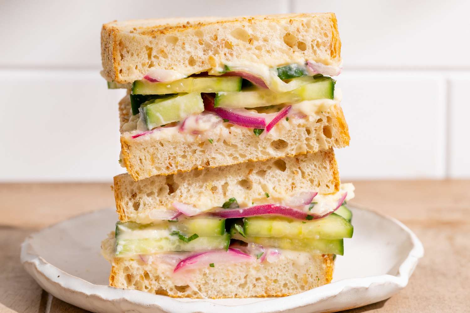 Stacked cucumber and red onion sandwiches on a white plate
