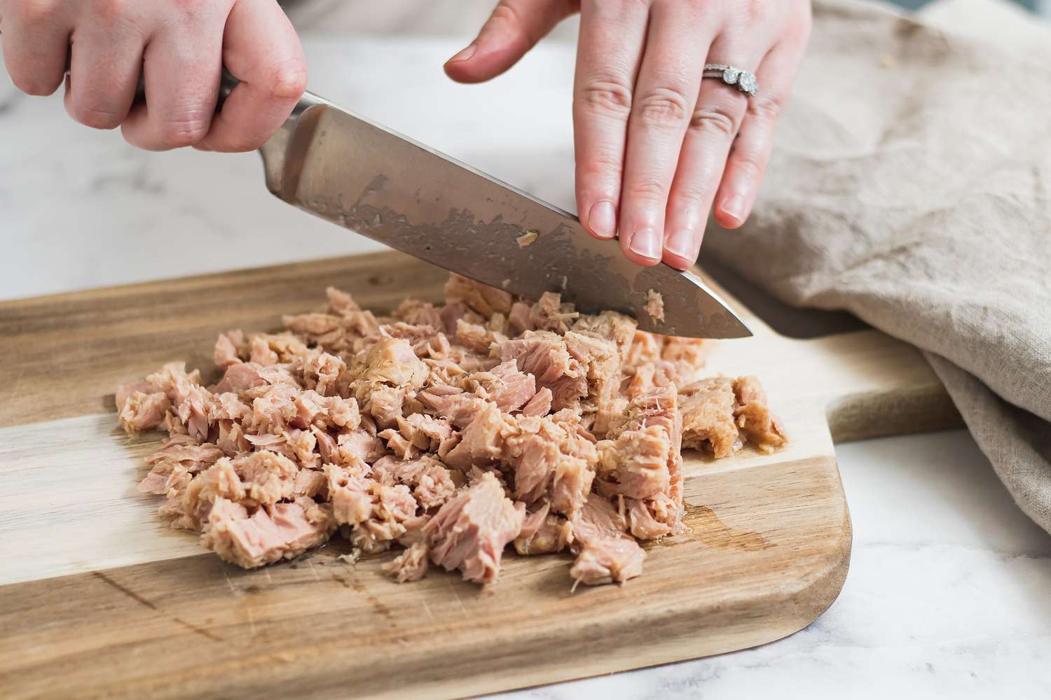 Chopping tuna on a cutting board to make a nicoise salad recipe.
