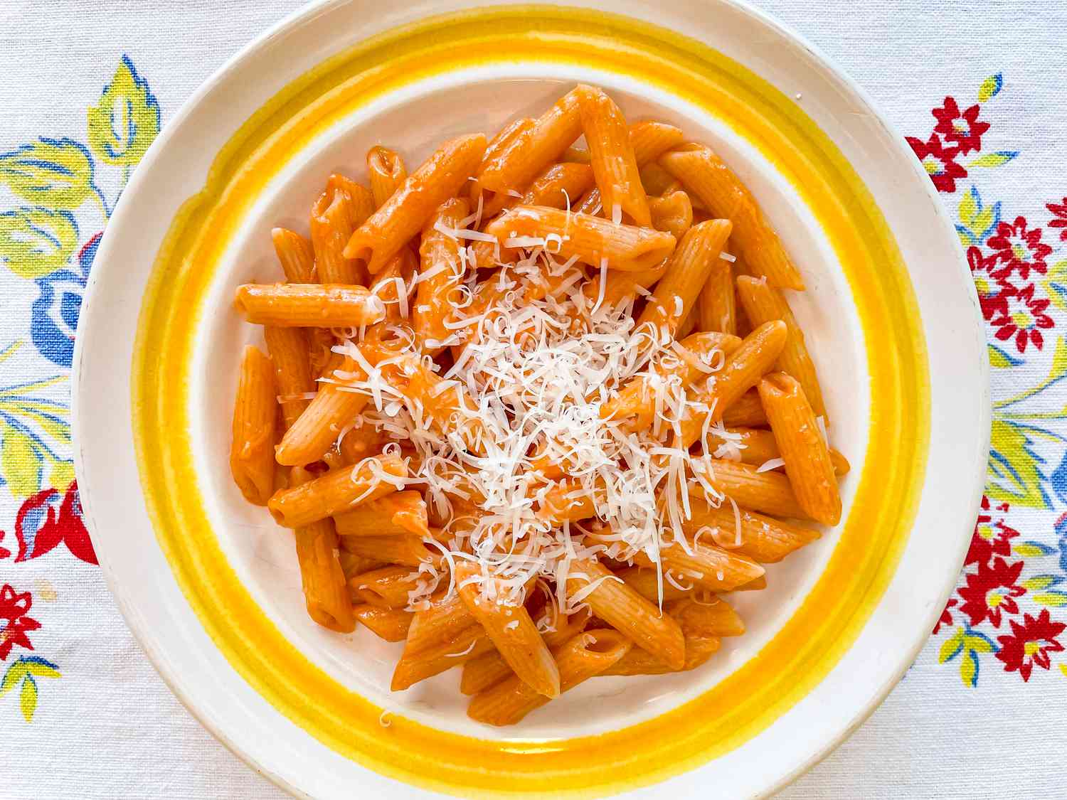 A shallow bowl filled with tomato sauce-slicked penne topped with finely shredded Parmesan