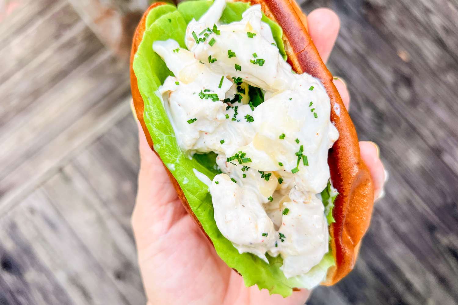 A hand holding a crab roll with lettuce and diced filling