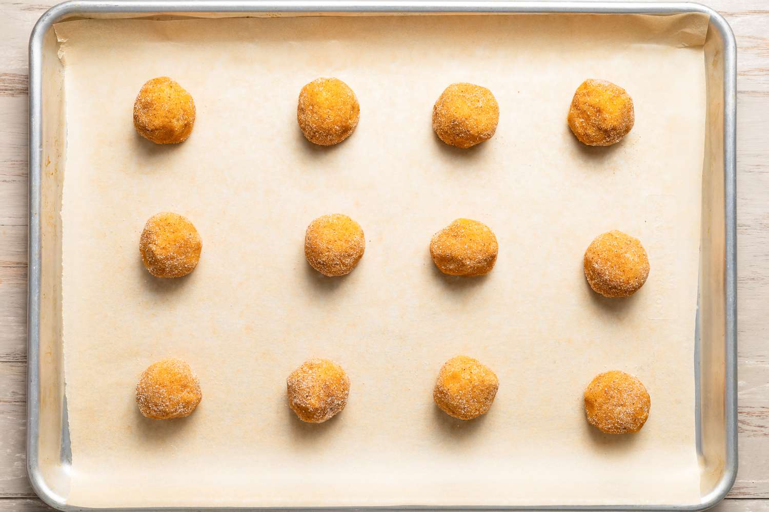 Balls of pumpkin spice sugar mixture covered pumpkin spice snickerdoodle cookies on a parchment paper lined baking sheet 