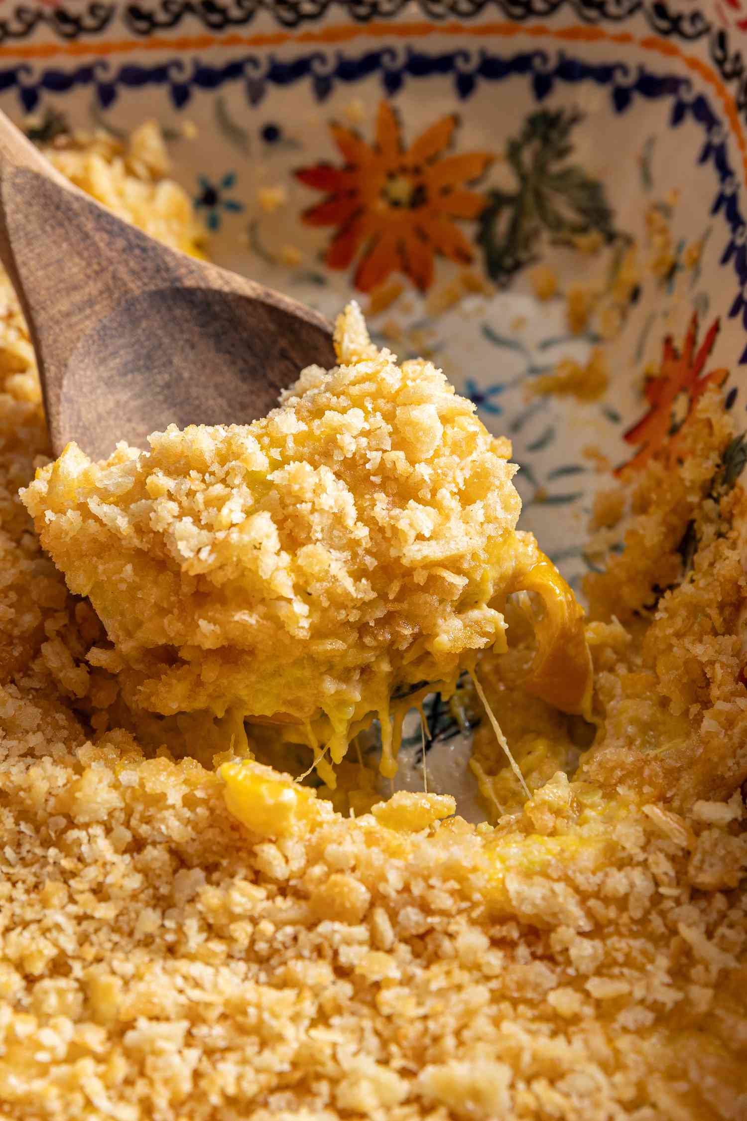 spoonful of squash casserole lifted from casserole dish using a wooden spoon