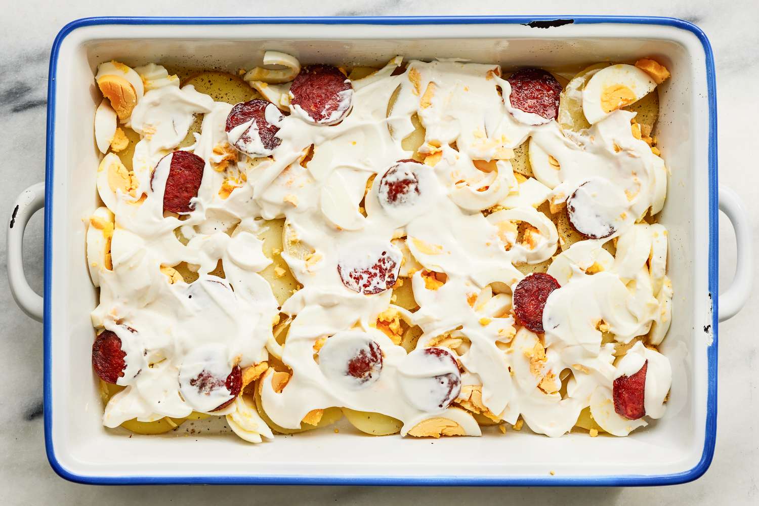 layers of Rakott Krumpli (Hungarian Potato Casserole) ingredients in a 9x13 casserole dish