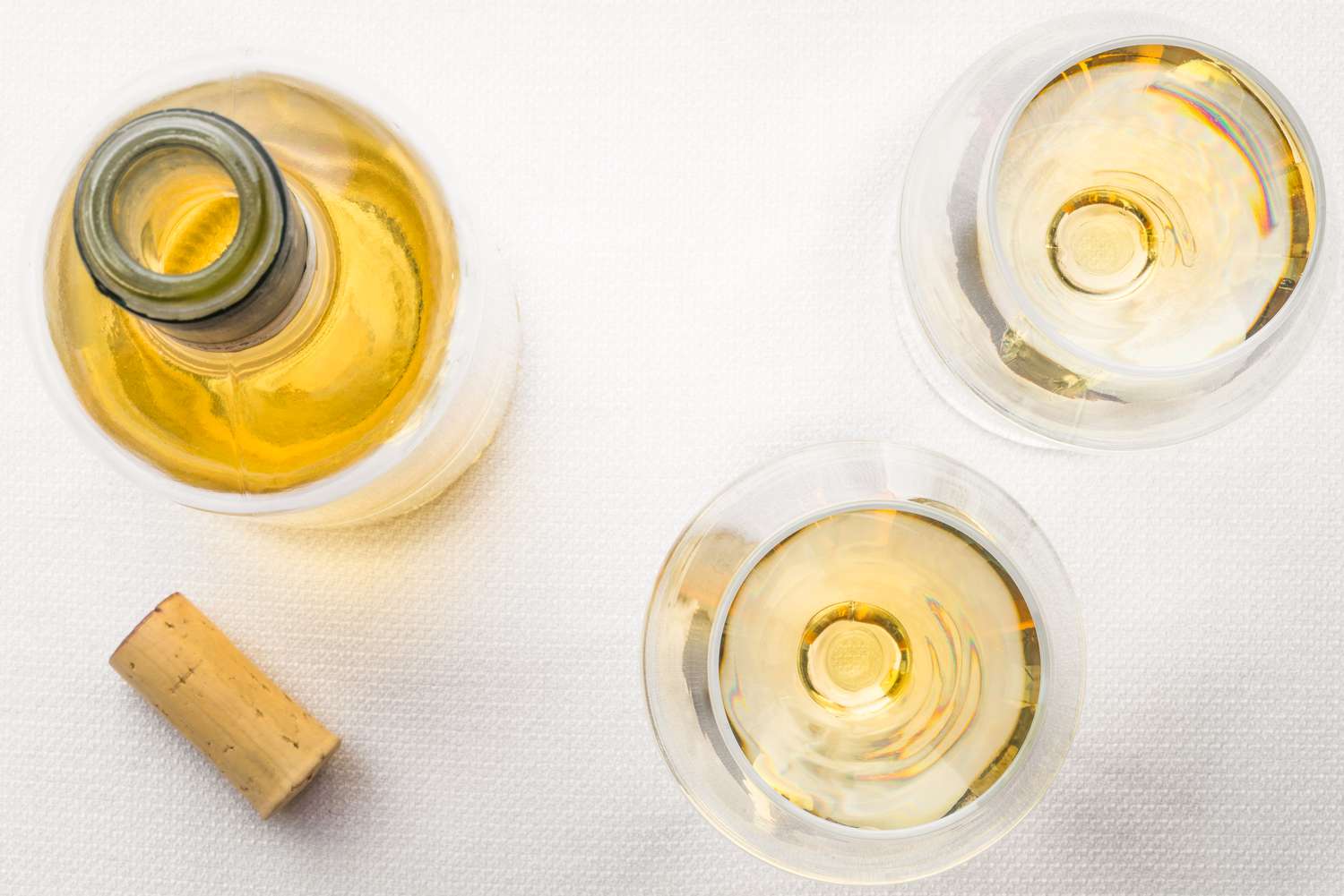 A top-down view of an open bottle of white wine next to two wine glasses with wine inside