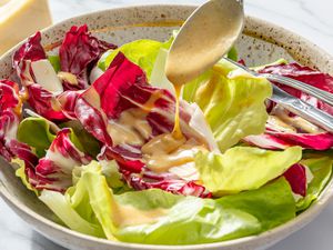 A bowl of salad with lettuce and radicchio leaves, a spoon is drizzling vinaigrette over the salad