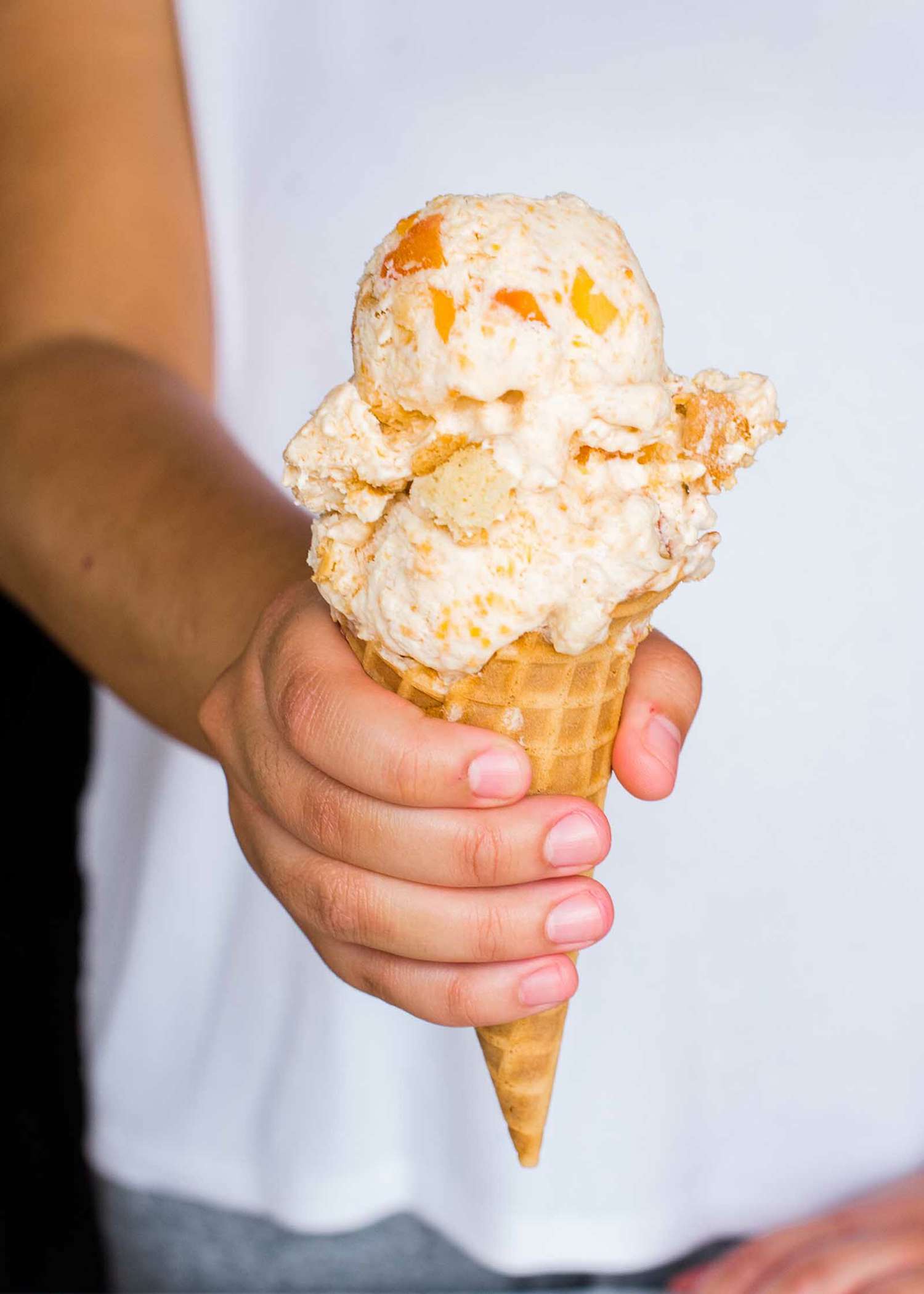 A hand holds a peach cobbler ice cream cone.