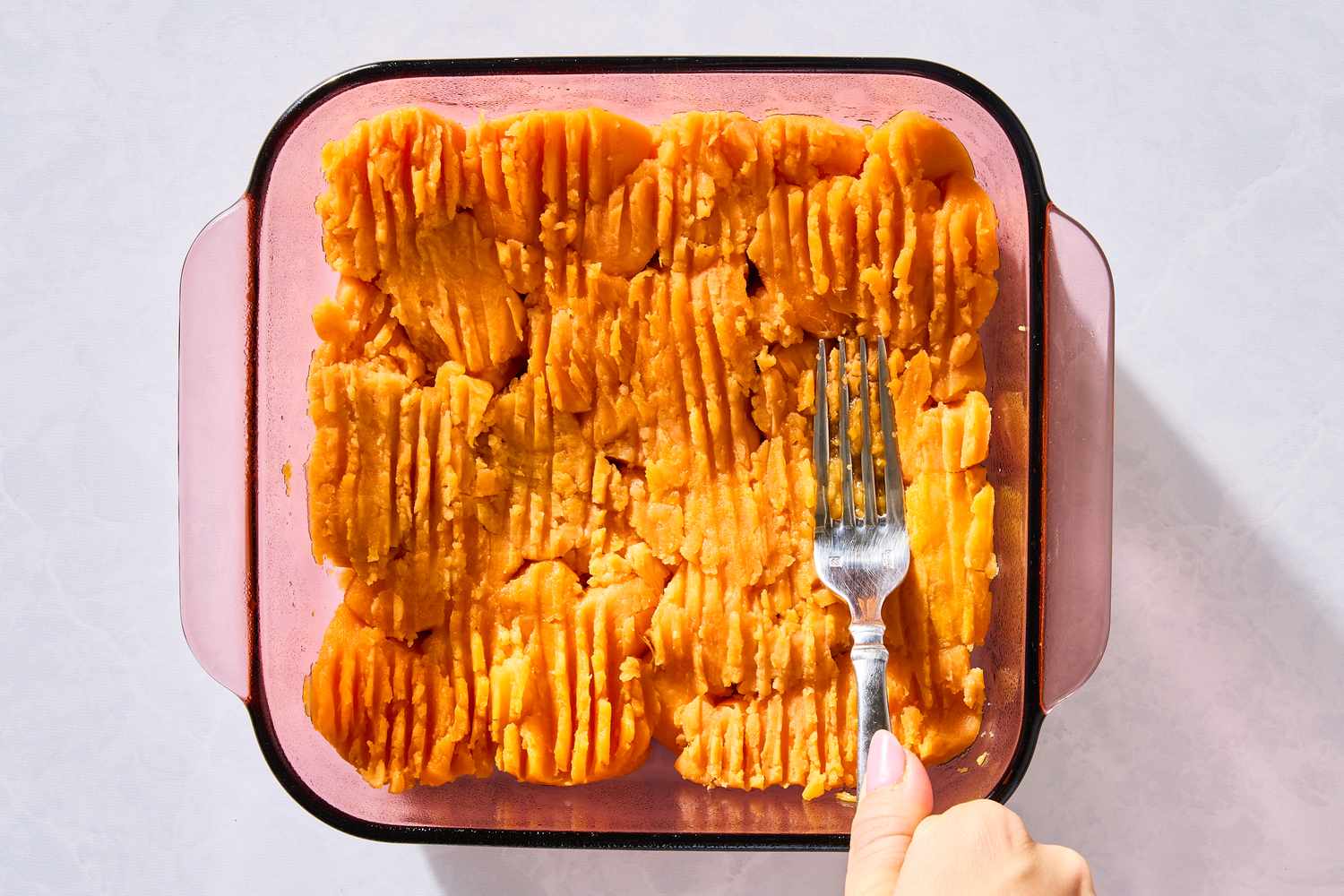 fork pressing canned yams into the bottom of a baking dish for 4-Ingredient Sweet Potato Dump Cake