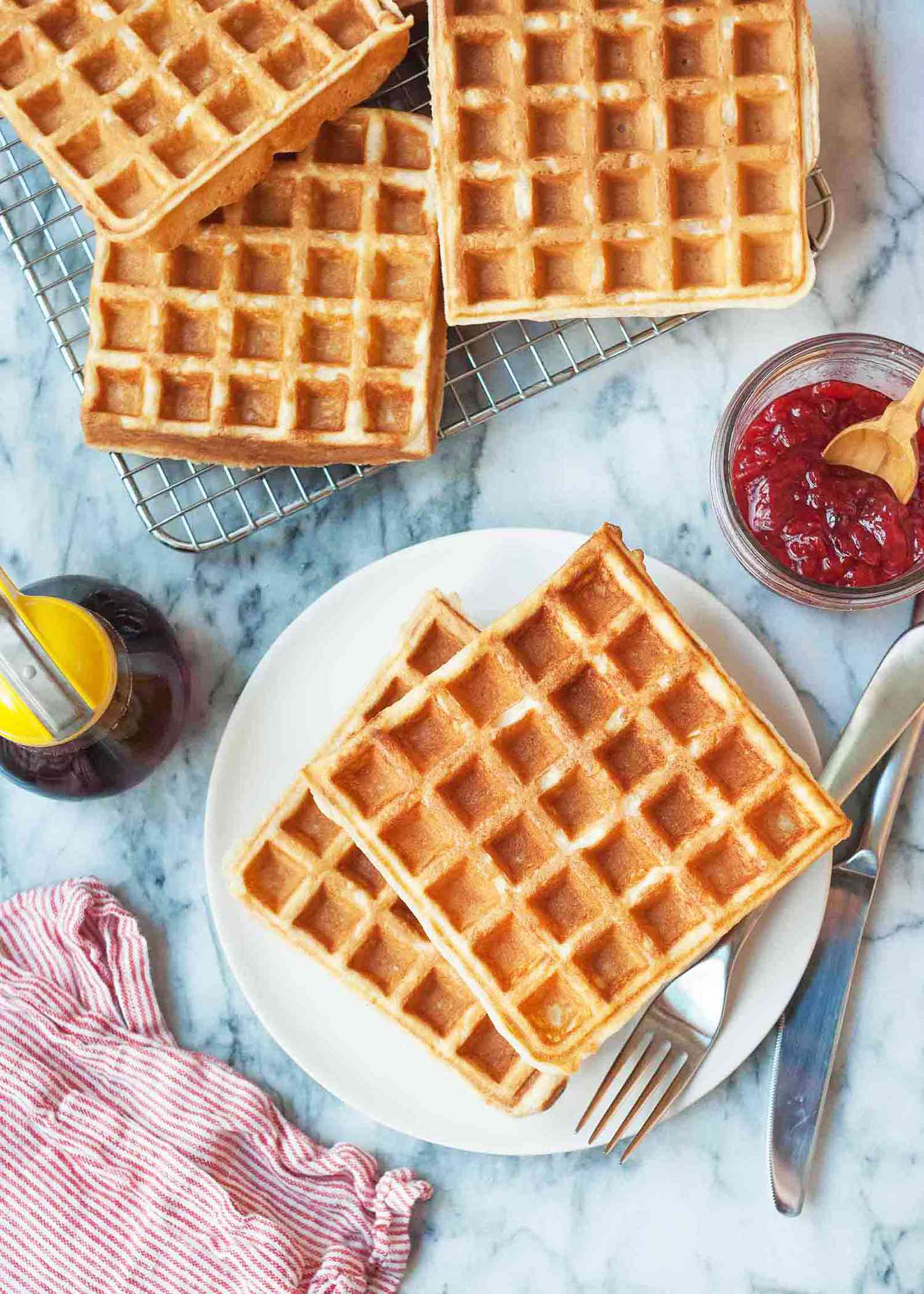 Buttermilk waffle recipe on a round plate with extra waffles on a cooling rack nearby