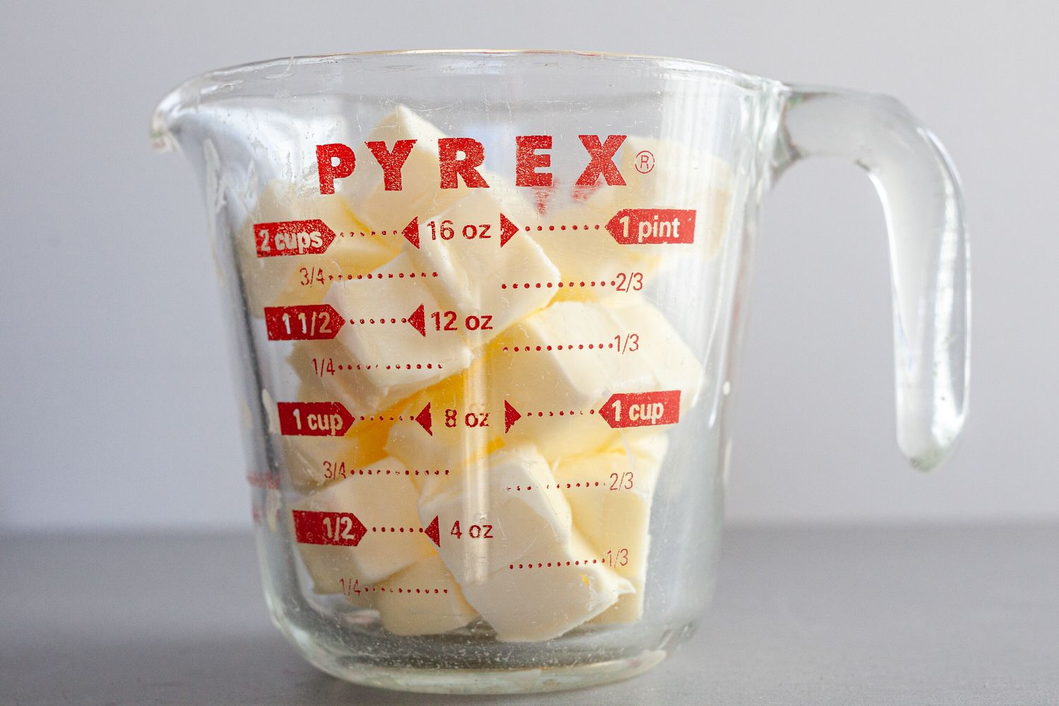 Side view of a liquid measuring cup with cubes of butter to to make béarnaise sauce.