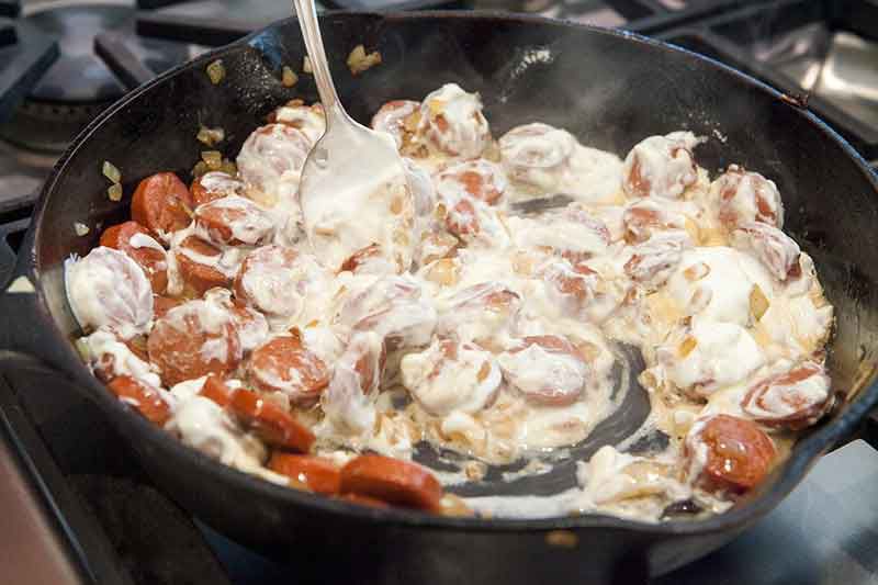 stroganoff sauce ingredients added to hot dogs in a skillet