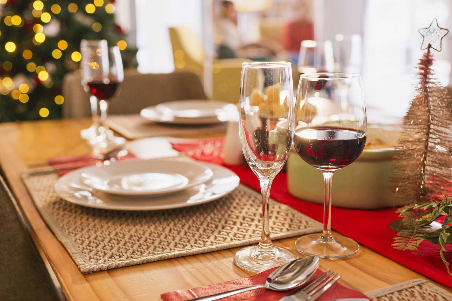 A festive dinner table set with wine glasses and plates with a Christmas tree in the background