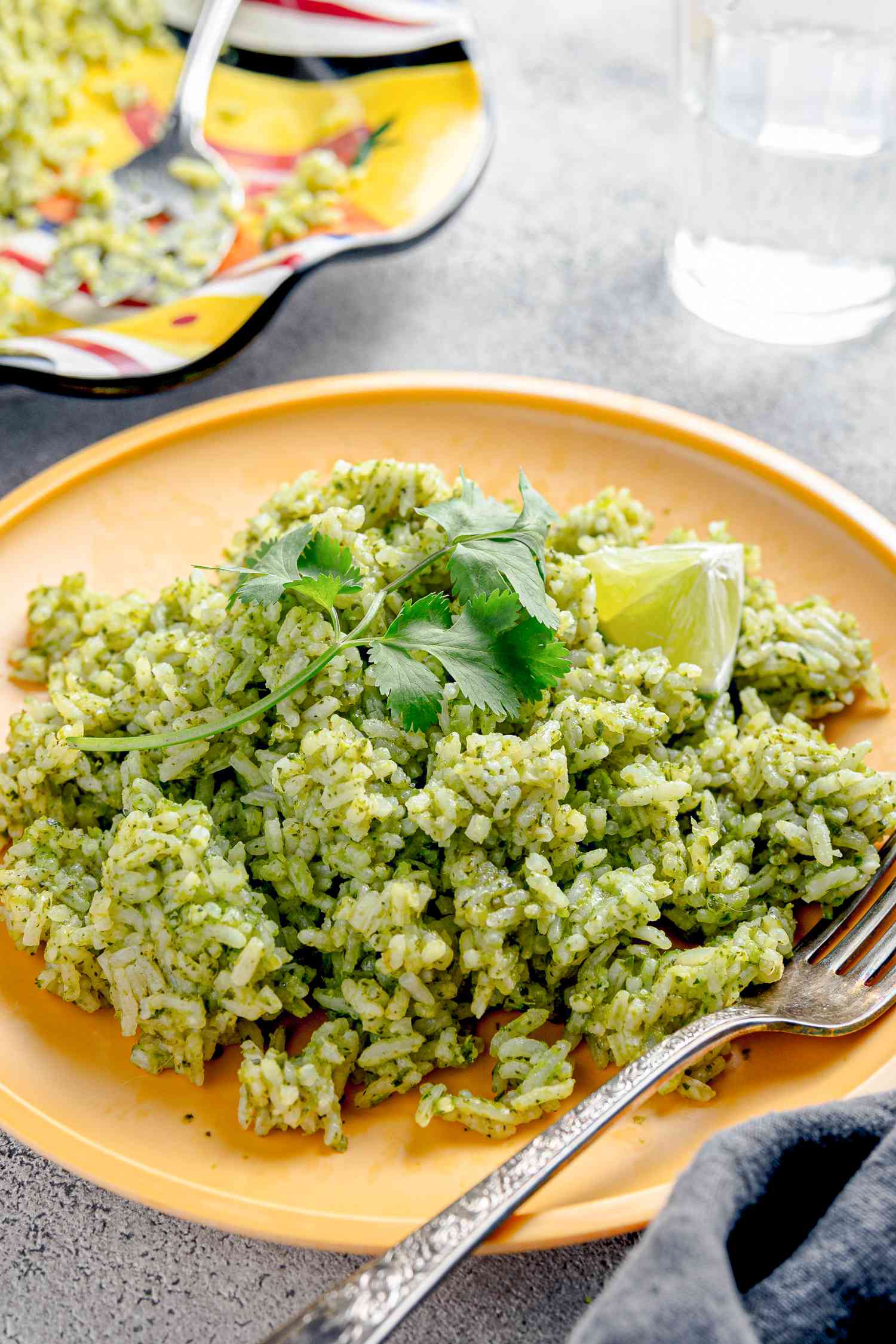 Microwave Arroz Verde on a Plate with a Fork Next to a Table Napkin, Glasses of Water, and a Plate with More