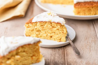 single slice of clementine cake on a small plate with a fork and the rest of the cake in the background