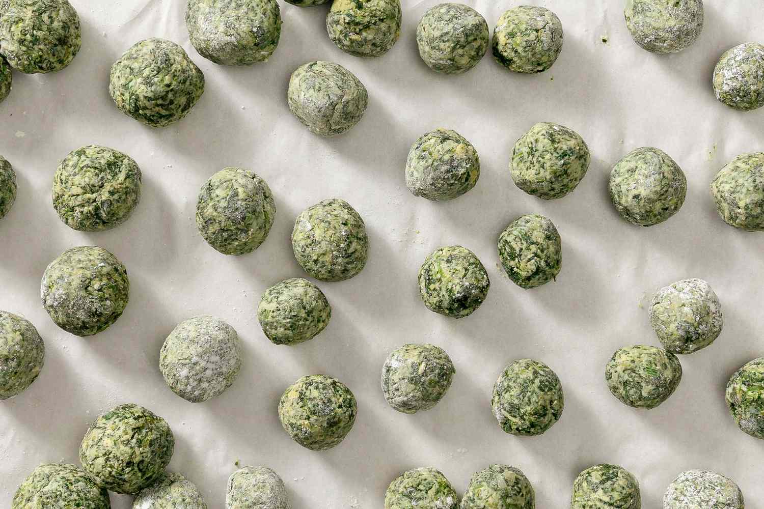 Overhead view of shaped dumplings on a parchment-lined baking sheet after freezing for Ravioli Gnudi recipe