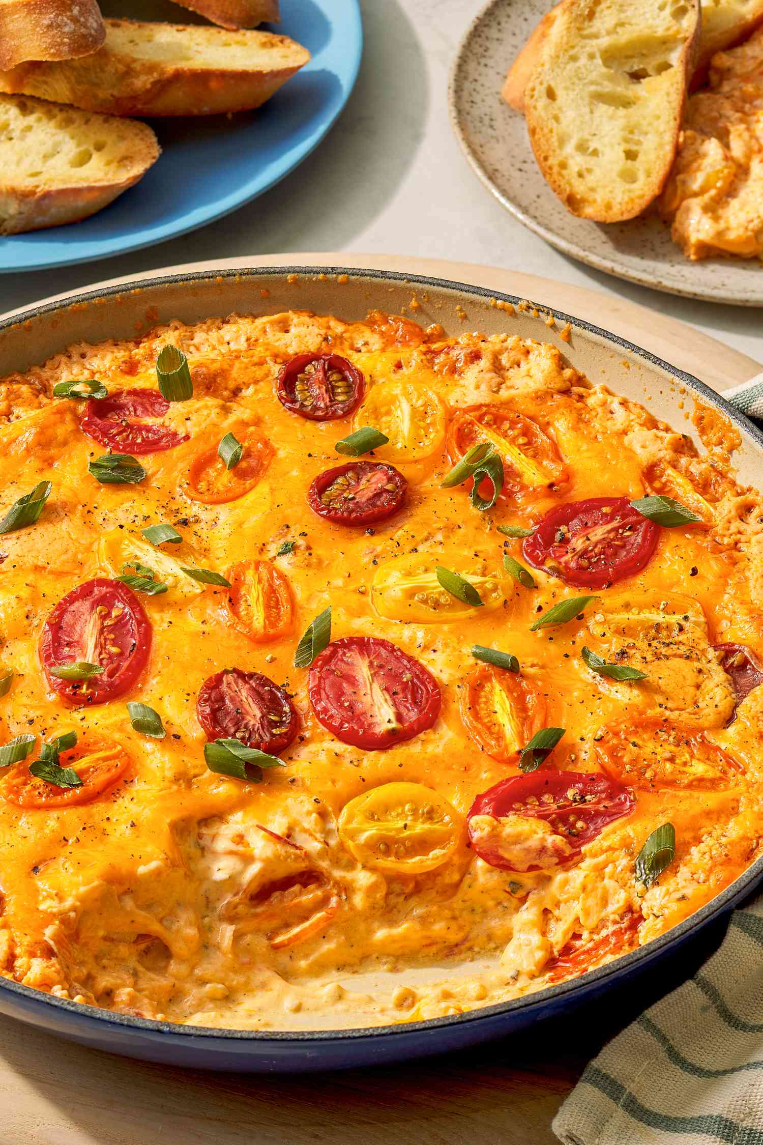 tomato pie dip in a pan and in the background, two plates with dip and toasted baguette slices