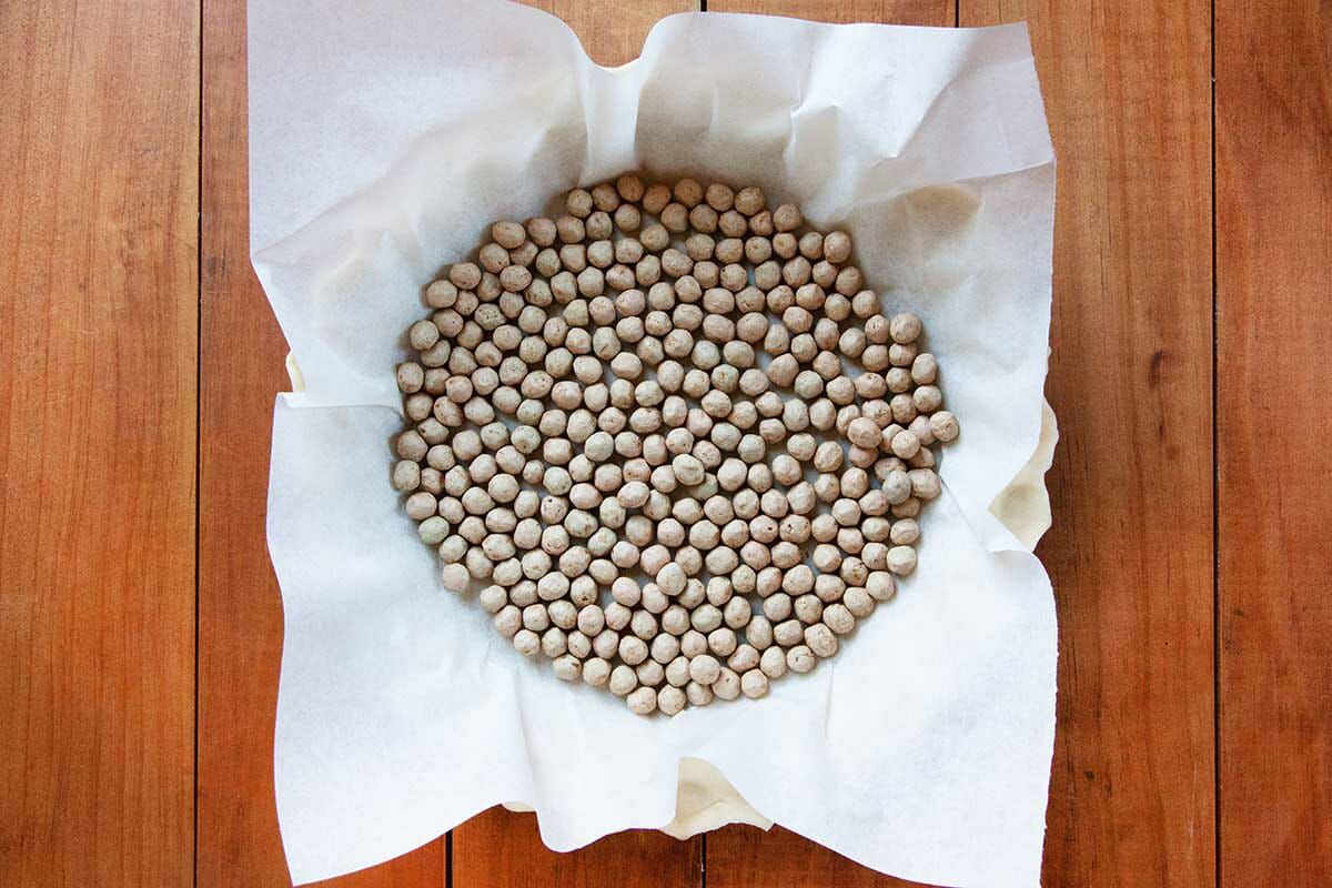 A pie crust is filled with pie weights to show how to make chess pie.