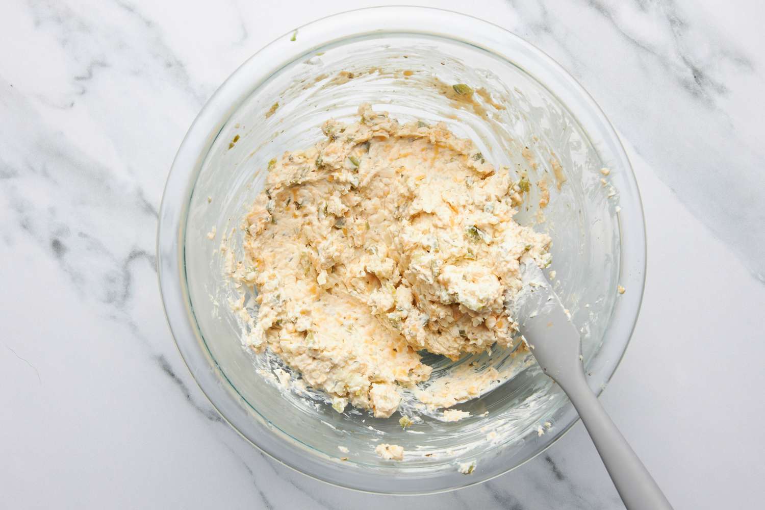 Cheeses for jalapeÃ±o popper grilled cheese mixed together in a bowl using a plastic spatula