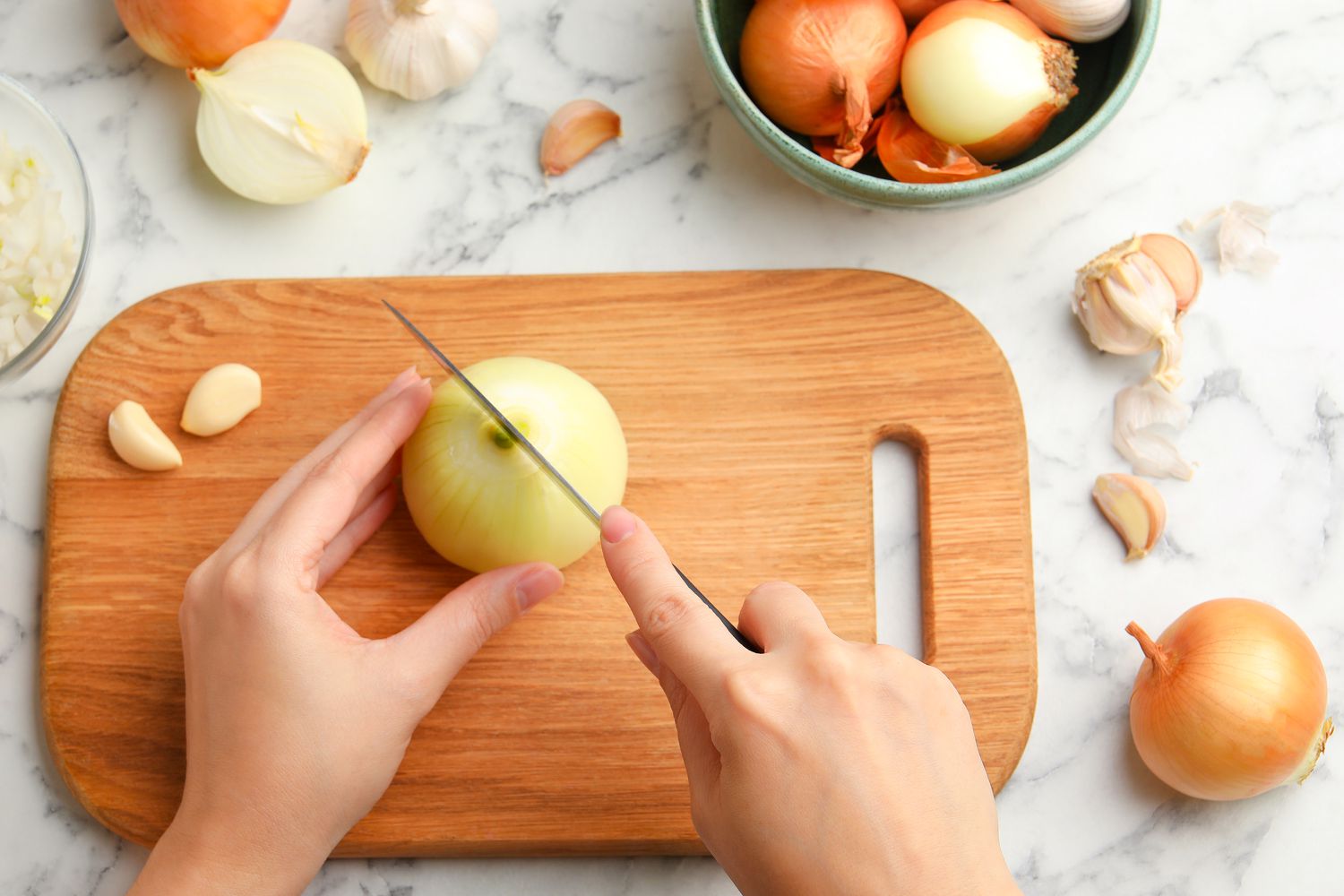 Hands cutting fresh onion on wooden board at white marble table