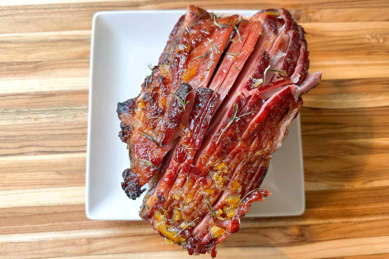 A sliced glazed ham showing rosemary in the glaze