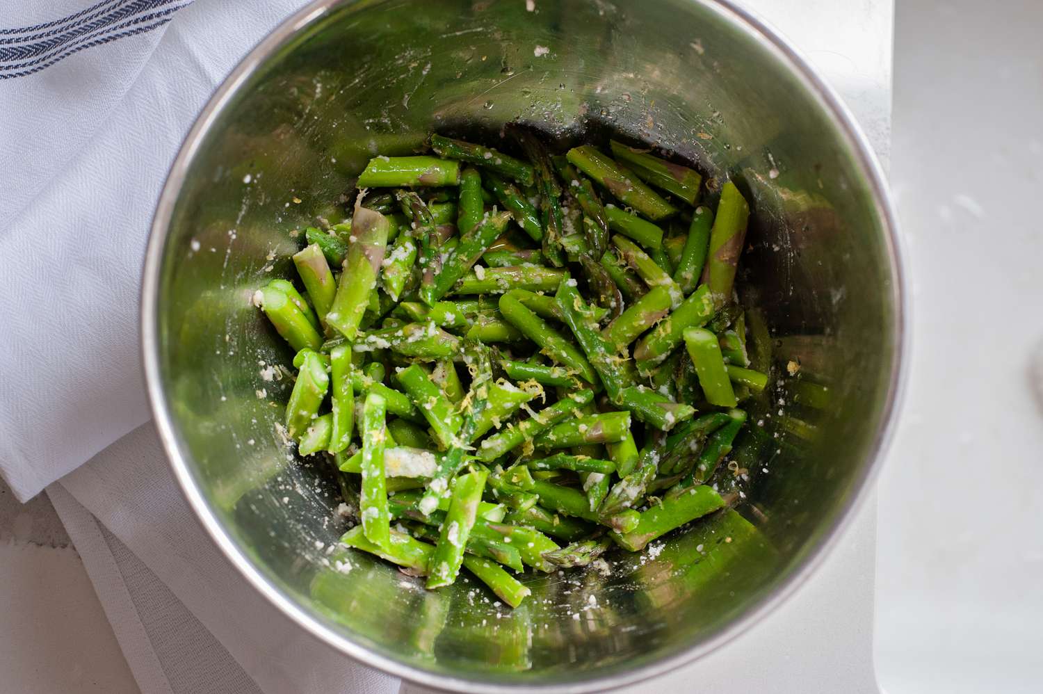 A metal bowl with asparagus pieces tossed with Parmesan