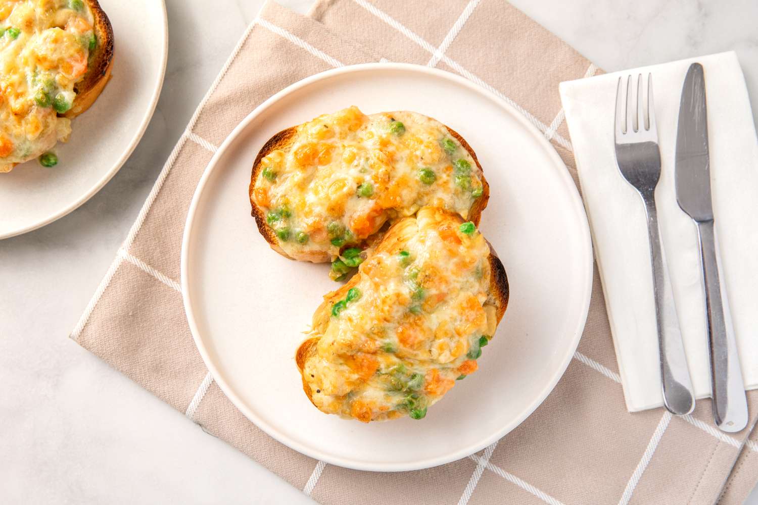 Two chicken pot pie toasts served on a white plate accompanied by a knife and fork on the side