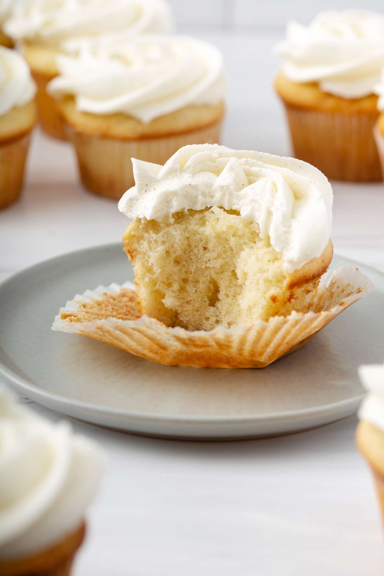 Side view of vanilla cupcakes from scratch with the center one with a bite out of it and set on a plate.