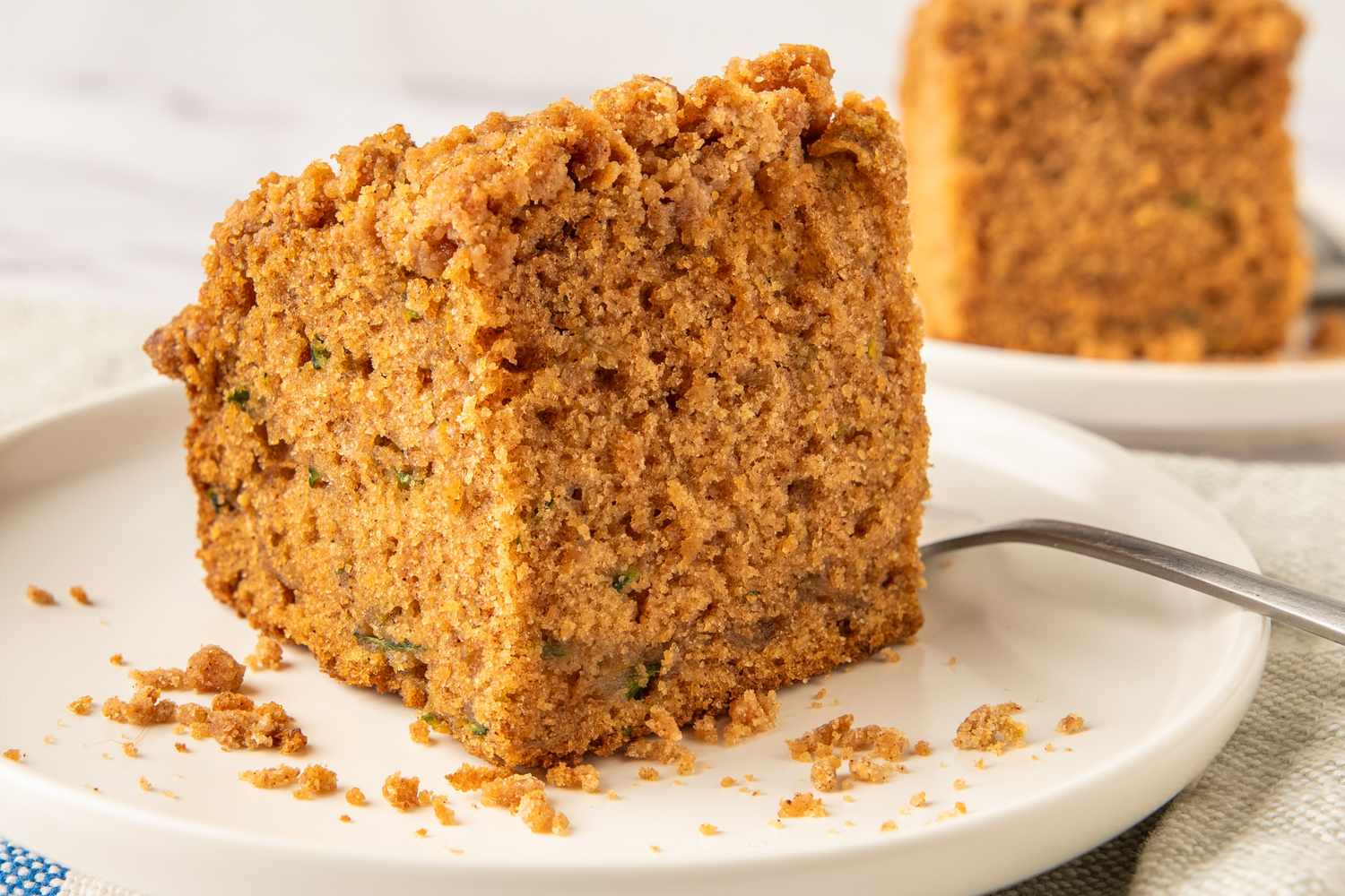 A slice of zucchini coffee cake with crumb topping on a plate with a fork