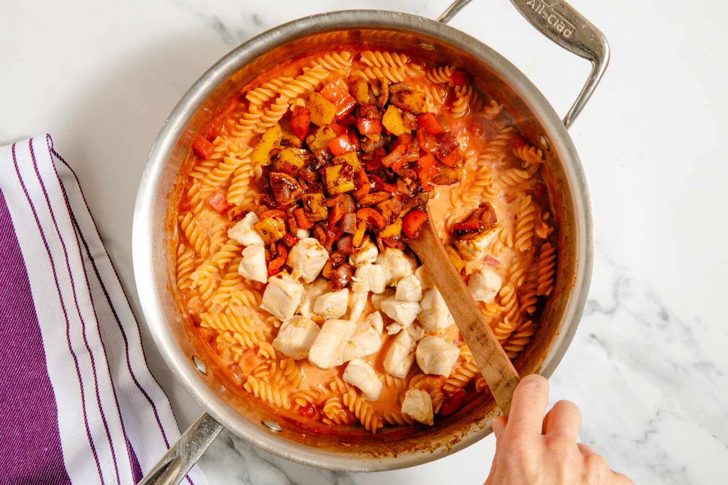 veggies and chicken added to pasta mixture in pan, hand stirring with wooden spoon for One-Pan Chicken Fajita Pasta
