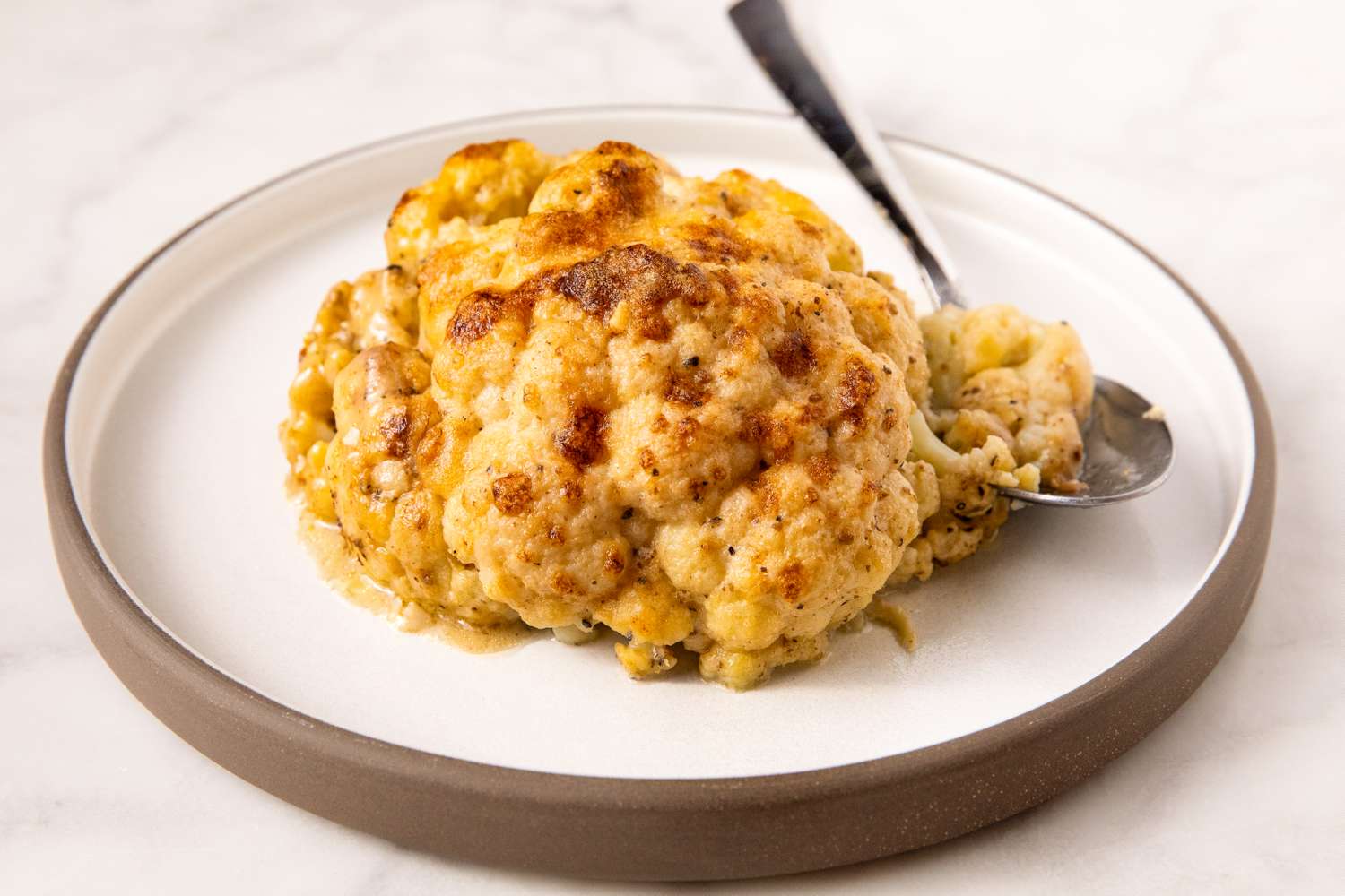 A baked whole cauliflower served on a plate with a spoon