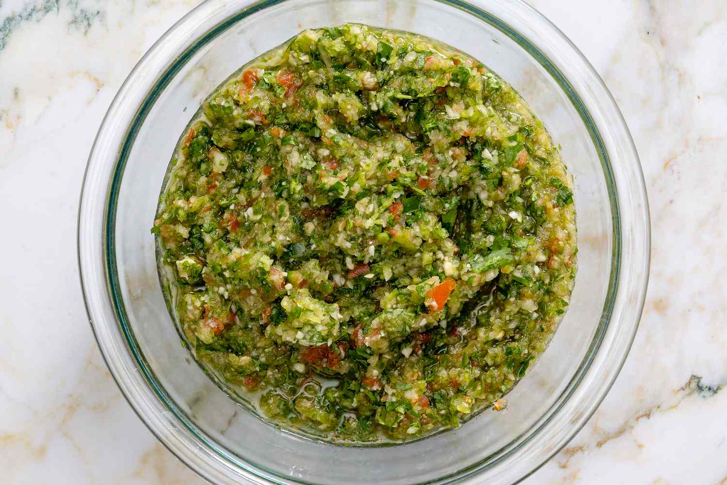 Overhead view of a clear glass bowl of sofrito after blending on a marble countertop for Easy Puerto Rican Picadillo recipe