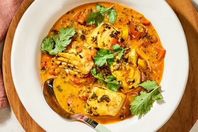 A bowl of moqueca Brazilian fish stew with fish pieces tomatoes herbs and broth garnished with cilantro