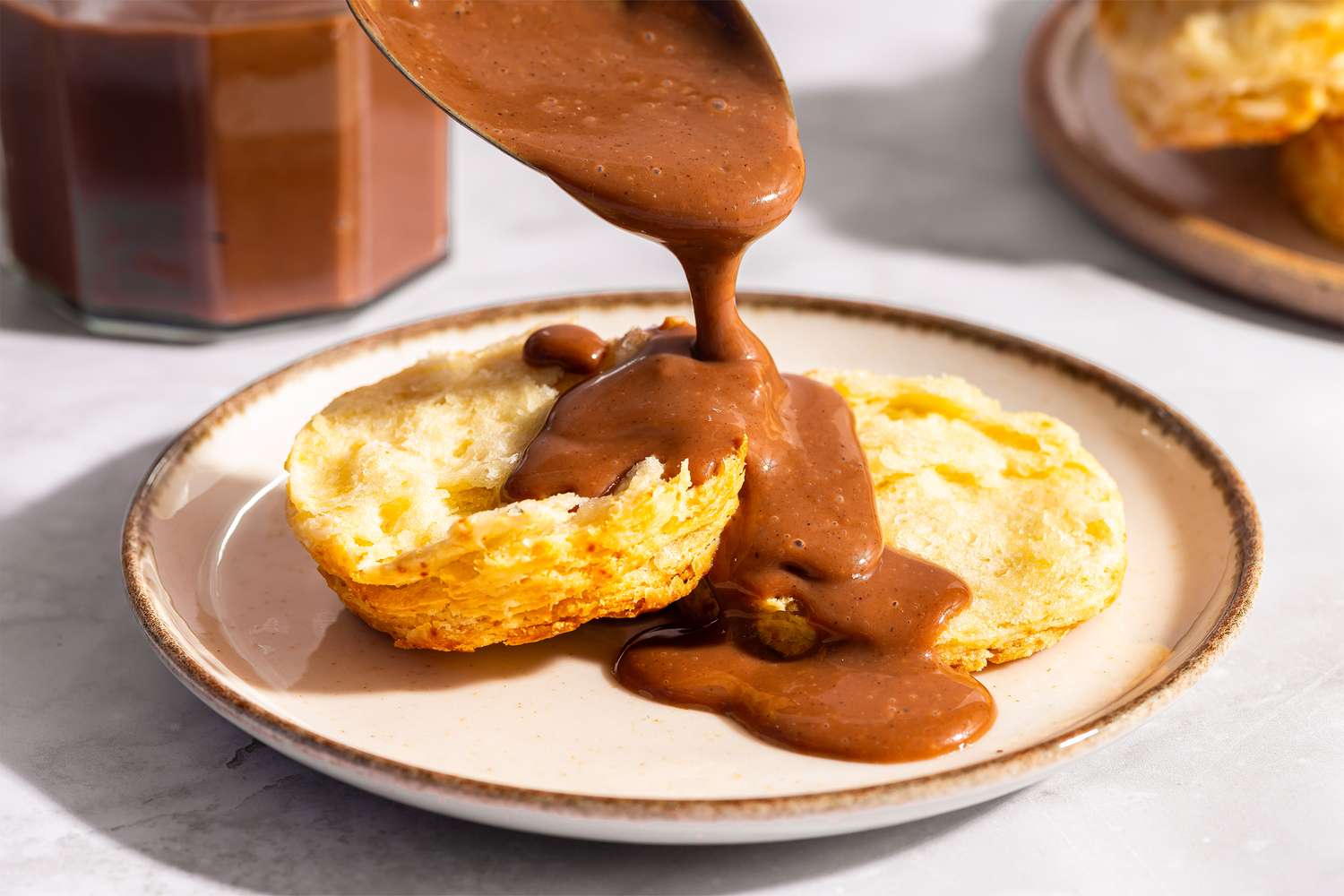 Biscuits topped with chocolate gravy being poured from a spoon onto a plate