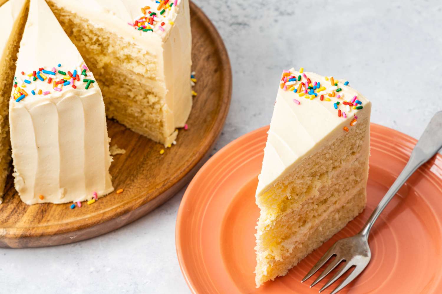 A sliced vanilla cake with frosting and sprinkles one slice is served on a plate with a fork