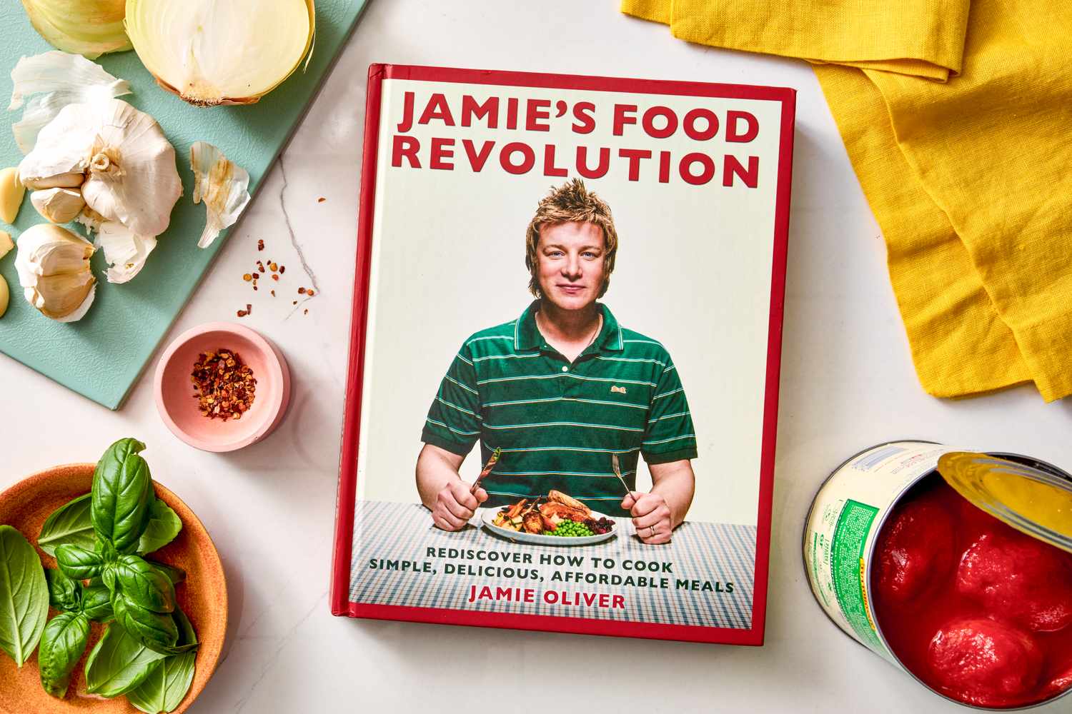 Jamie Olivers cookbook titled Jamies Food Revolution surrounded by cooking ingredients