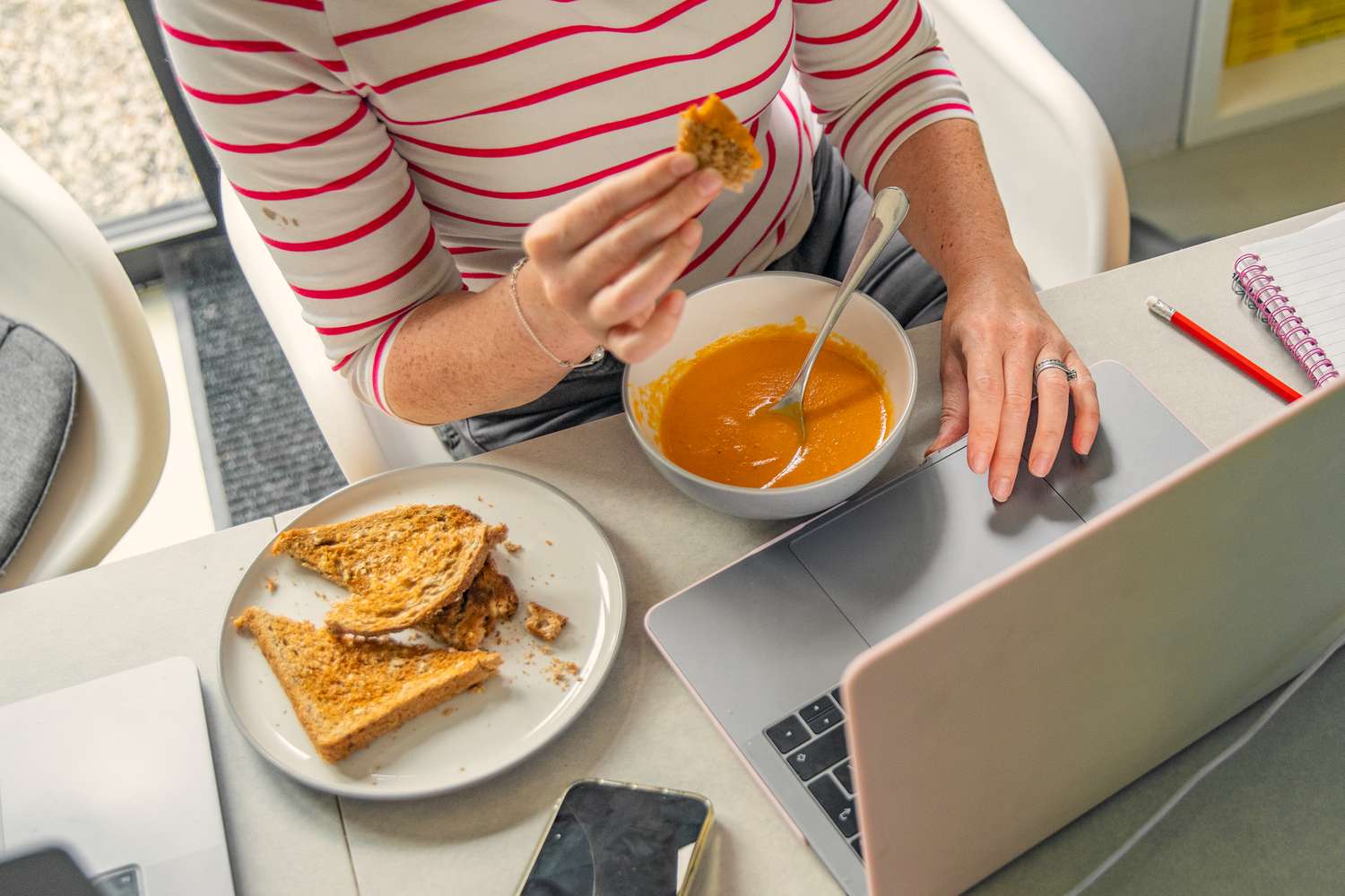 Person eating soup and toast while working on a laptop
