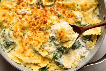 Cheesy spinach and artichoke ravioli cooked in a pan with a wooden spoon