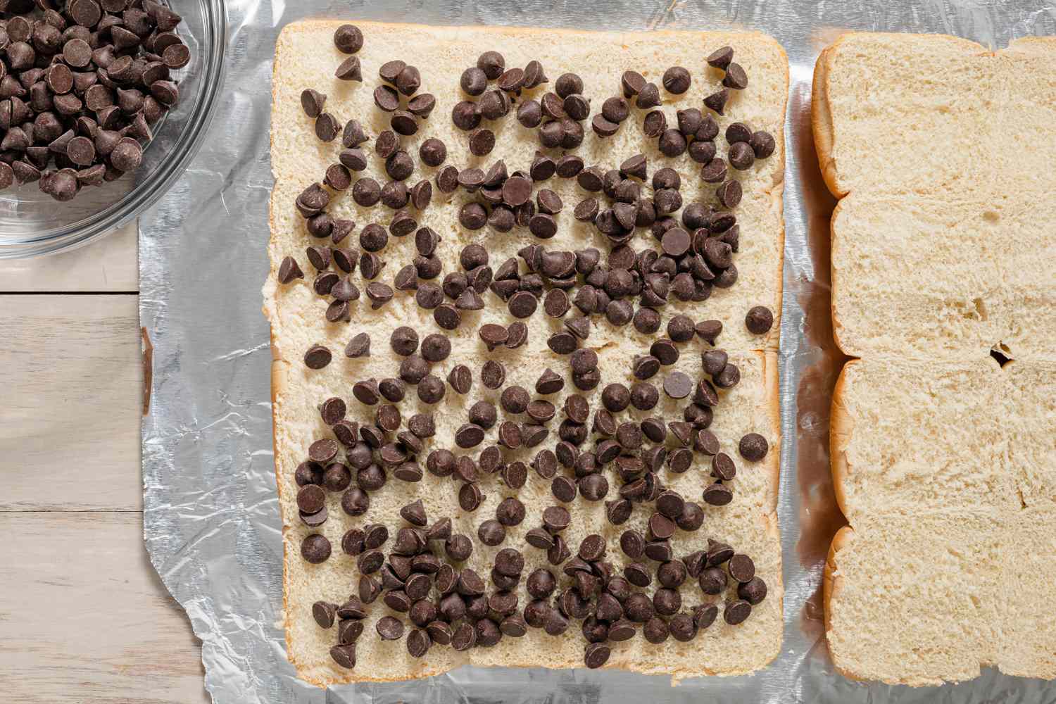 Chocolate Chips Spread Onto One of the Halved Slices. On the Left, a Bowl With More Chocolate Chips and on the Right, the Other Halved Slider Loaf for Grilled S'mores Slider Recipe