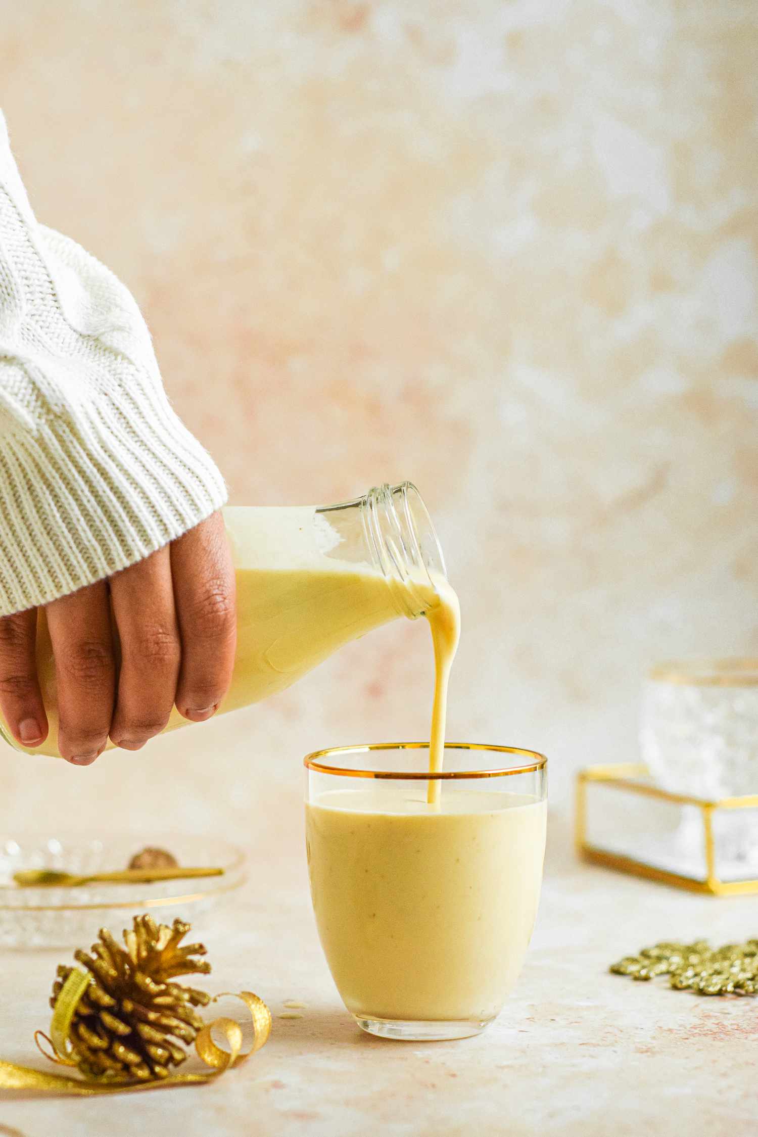 Pouring traditional egg nog from a glass jar into a gold rimmed glass.