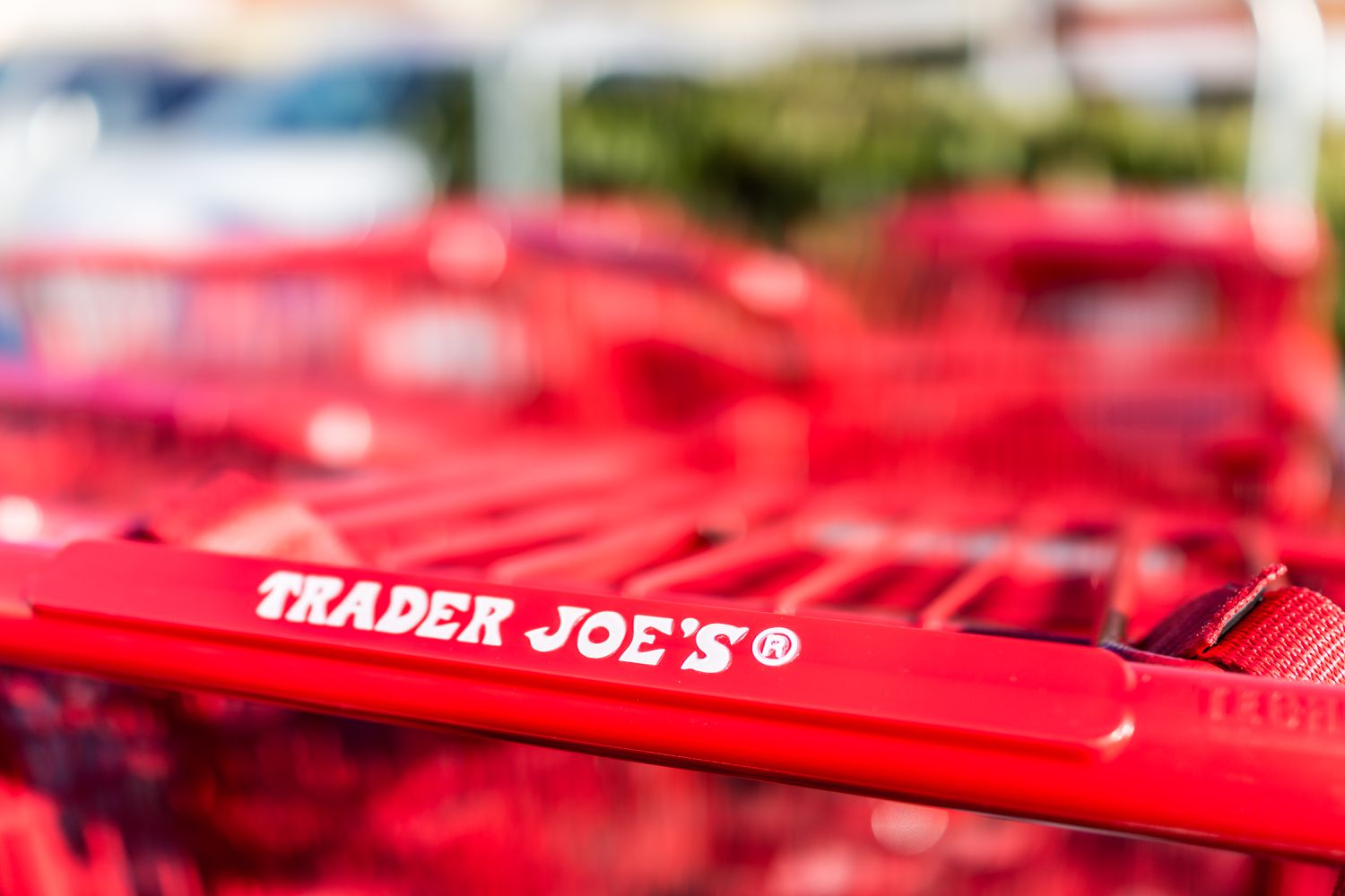 Closeup view of the bright red handle on a Trader Joe's shopping cart with a blurred background